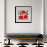 Framed artwork of red cherries on a checkered background above a black bench with wooden legs.