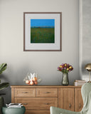 Framed artwork on a wall above a wooden cabinet with decorative items.