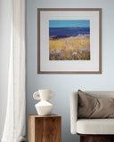 Framed artwork of a coastal scene with a vase and sofa in a room.