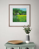 Framed painting of a landscape with a house on a wall above a green cabinet with decorative items.