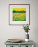 Framed painting of a field with flowers on a wall above a green cabinet with decorative items.