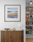 Framed beach scene art on a wall above a wooden sideboard with decor items.