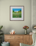 Framed artwork of a landscape on a wall above a wooden cabinet with decorative items.