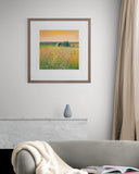Framed artwork of a field with a house on a wall above a sofa.