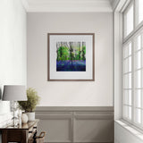 Framed artwork of a forest scene on a wall in a room with a desk and window.