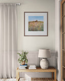 Framed artwork of a field on a wall above a wooden bench with decor items.