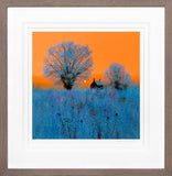 Framed artwork of a sunset over a field with trees and a house.