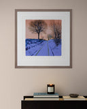 Framed artwork of a snowy landscape on a wall above a table with a candle and small bowl.
