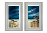 A pair of framed vertical beach landscape prints side by side. The artwork depicts a dramatic dark blue and purple stormy sky over a sandy beach with ocean waves and rocky shoreline.