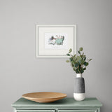 framed artwork on grey wall above a green wooden table.