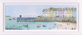 A framed pastel art print depicting a coastal harbor scene with colorful buildings, boats, a pier, and a sandy beach under a pale sky.
