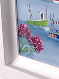 A close-up of a framed painting showing pink flowers in the foreground, blue water, and small boats, with a white painted frame visible around the artwork.