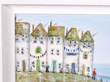A framed painting depicting a row of white seaside cottages with green and brown roofs, small figures standing in front, and a pale blue sky and sea in the background.