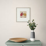 Framed artwork on a wall above a table with a vase and plate.