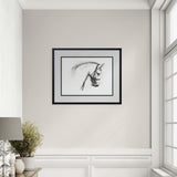 Framed black and white artwork of a horse's head on a wall in a room with a window and lamp.