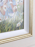 Framed artwork of a person sitting in a field with daisies on a white wall.