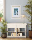 White bookshelf with books against a light blue wall with a framed picture.