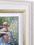 Framed artwork of two girls in hats sitting in a field of flowers.