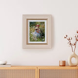 Framed artwork of two children in a garden on a wall above a wooden cabinet.