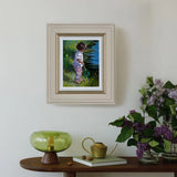 Framed painting of a child in a garden on a wall above a wooden table with decorative items.