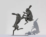 Bronze sculpture of two boxing hares with a white background