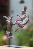 Bronze sculpture of two figures in mid-air against a blurred natural background