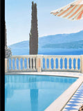 Pool area with a striped umbrella, cypress tree, and mountain view.