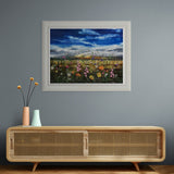 summer meadow of yellow, pink and orange florals against blue sky on grey blue wall above a wooden sideboard.