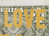A close-up of a dollar bill with the word LOVE printed in large gold letters across it.