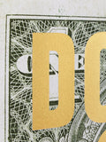 A close-up of a gold foil letter 'D' overlaid on a black and white dollar bill pattern background.