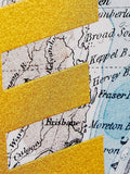A close-up of a decorative paper or card design featuring a vintage map background with diagonal strips of glittery gold tape overlay.