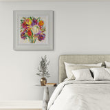 Bedroom with a floral painting on the wall, bed with pillows, and small table with plant and books.