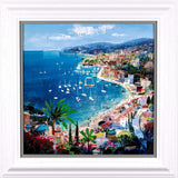 A framed coastal landscape painting featuring a blue harbor with many sailboats, a densely built seaside town, mountains in the background, palm trees, and bright flowers in the foreground, presented in a white frame.