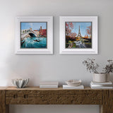 two cityscape artwork on light grey wall above a wooden sideboard.