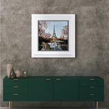 cityscape artwork of eiffel tower surrounded by red trees framed in white on grey textured wall above dark green sideboard.