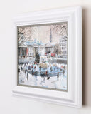 Framed artwork of a snowy city scene with people skating on an ice rink.