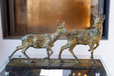 Bronze sculpture of two deer on a reflective surface with a blurred background