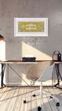 A framed art print with a yellow and green patterned background and the text 'WHAT YOU SAY IS THE message OF LIFE' in gold, hanging on a textured gray wall above a wooden desk with a chair and typewriter.