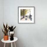 Framed print of a park scene on a wall above a small table with plants.  Jo Quigley limited edition art print in room setting