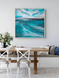 A square framed painting of turquoise ocean waves under a cloudy sky, displayed on a wall