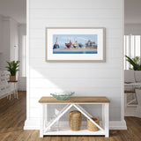 Framed artwork of a harbor scene on a wall above a wooden bench.