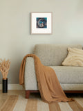 A framed square art print with a white mat hangs on a light sage green wall above a modern light gray sofa