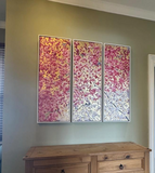 Three floral wall art pieces on a green wall above a wooden cabinet.