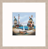 A framed art print featuring a whimsical coastal scene with colorful houses, a lighthouse, blue water, and a small sailboat, presented with a whitewashed oak frame.