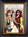 Framed Day of the Dead style art print featuring a white horse with decorative floral markings and a woman with red hair and sugar skull makeup, shown in an ornate black frame with gold inner trim.